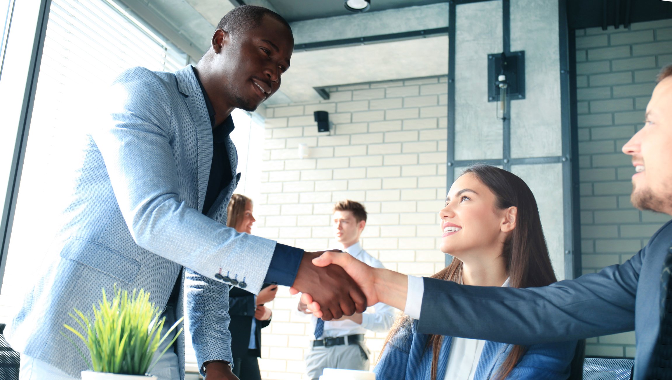 A man shakes the hand of another man while a woman watches him.