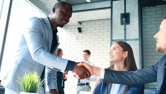 A man shakes the hand of another man while a woman watches him.