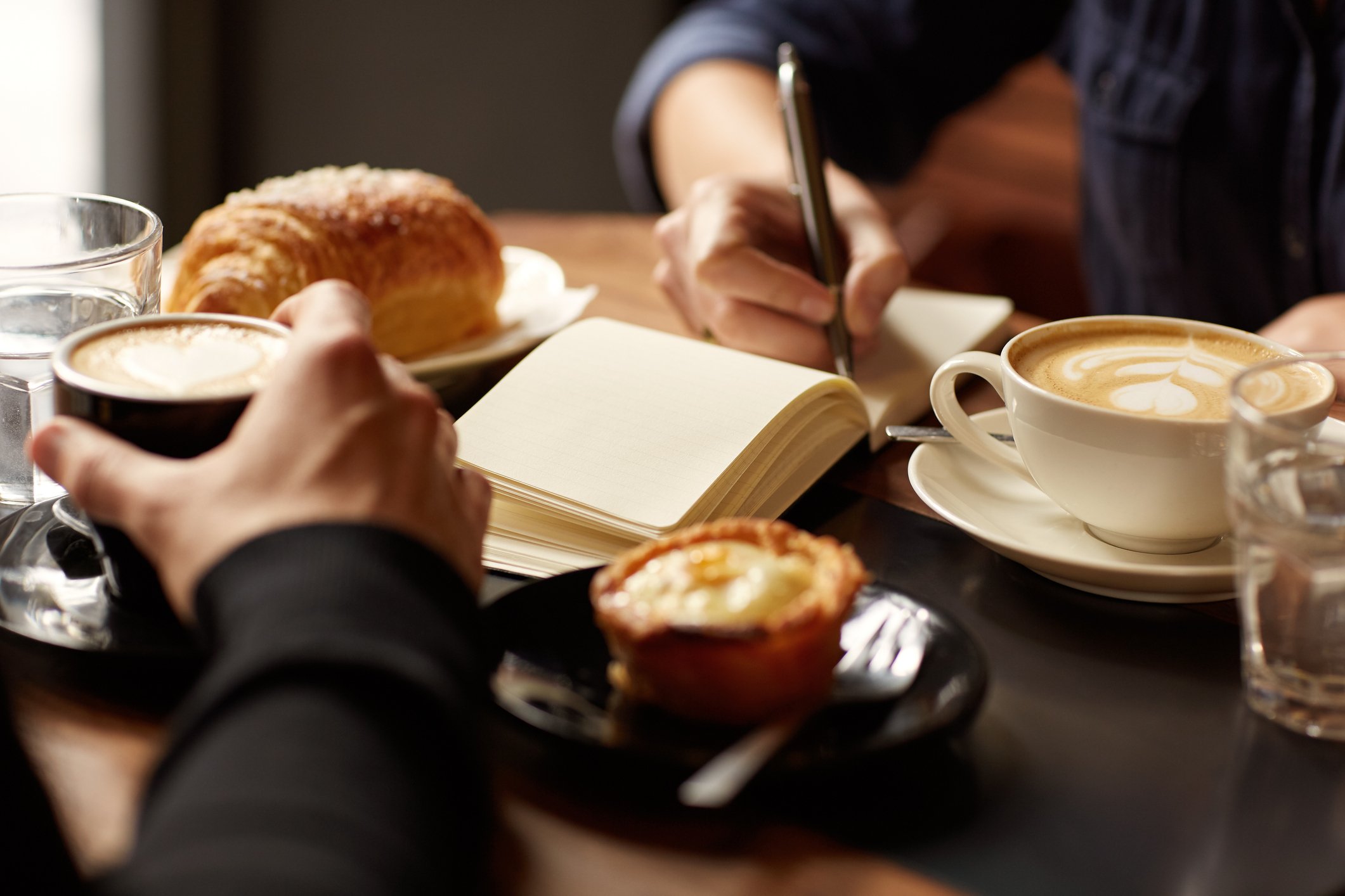 Pastries and coffee are seen at a table between two people facing each other.