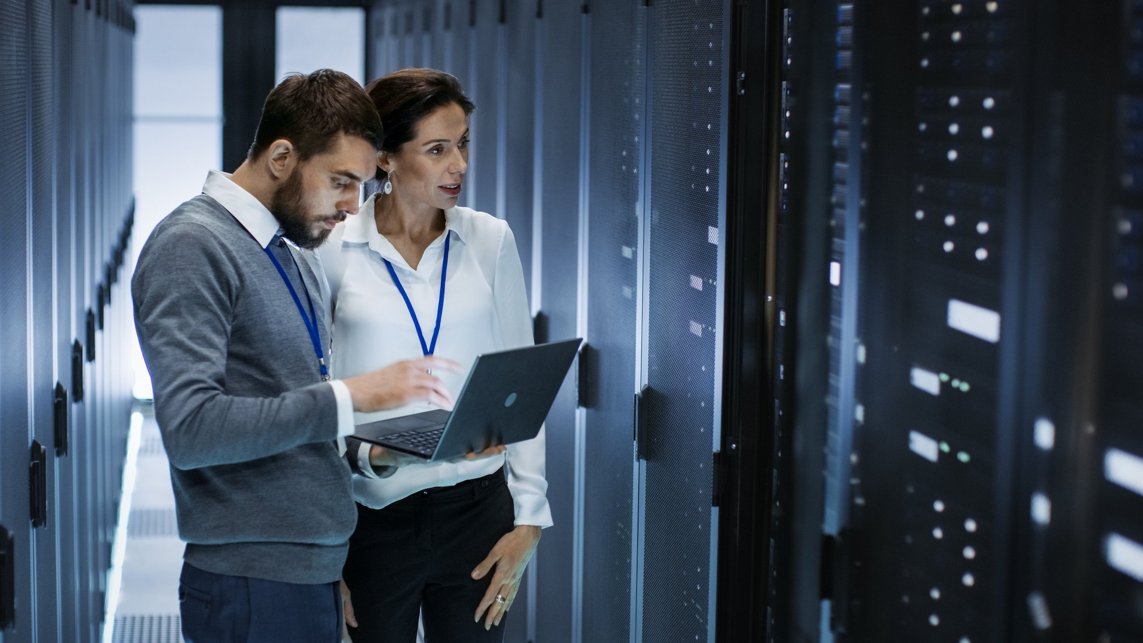 A man looks at laptop while discussing with a woman in a server room