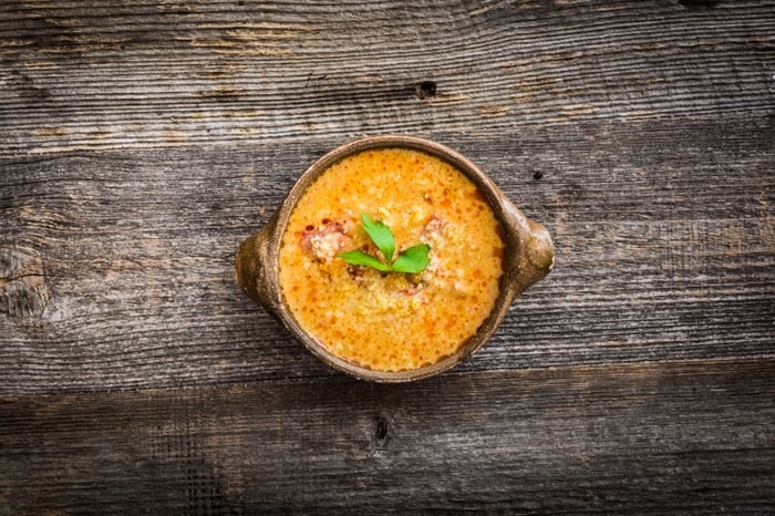 Rich yellow-orange queso in small crockpot style bowl on wooden table.