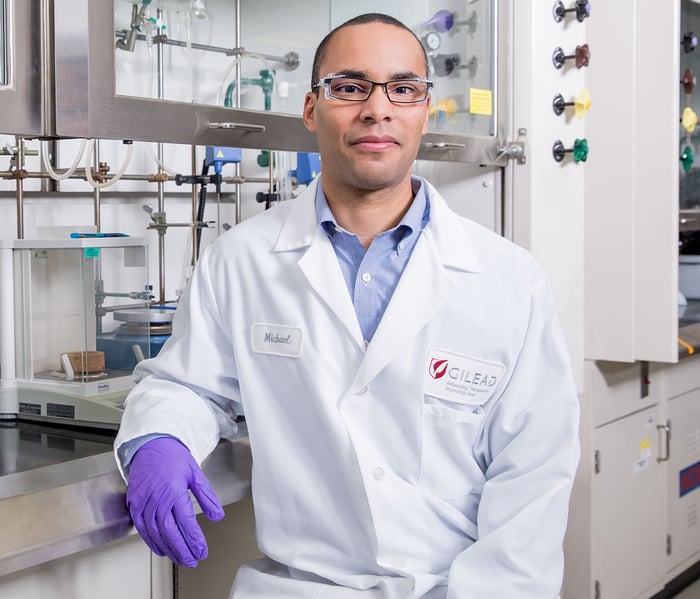 Gilead Sciences lab technician wearing a white lab coat and purple gloves, in a lab.