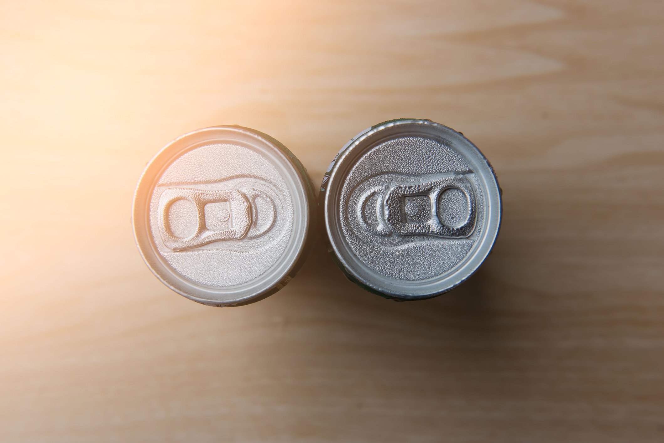 Two beverage cans sit facing each other on a table, as seen from above.