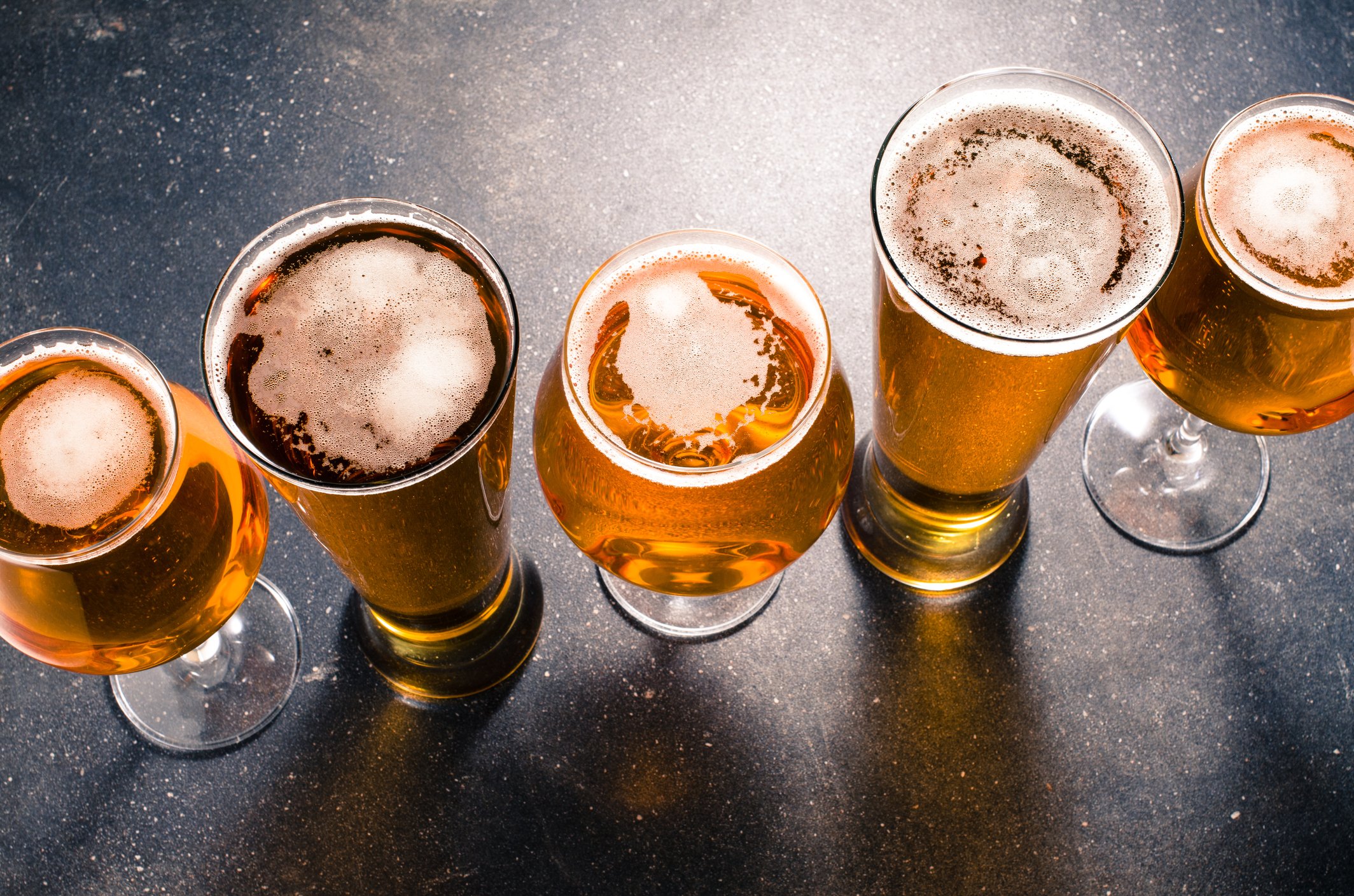Five beers in different glasses sitting on a counter.