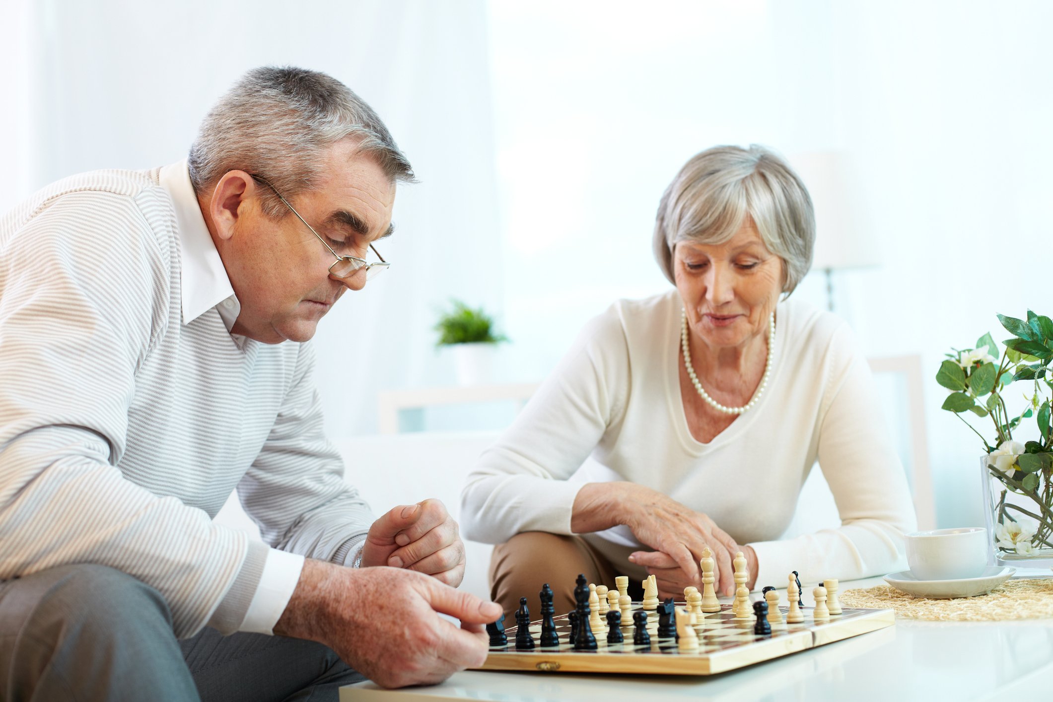 An older couple sits at a table playing chess.
