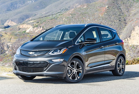 A black 2017 Chevrolet Bolt EV hatchback parked near a mountain road in bright sunlight.