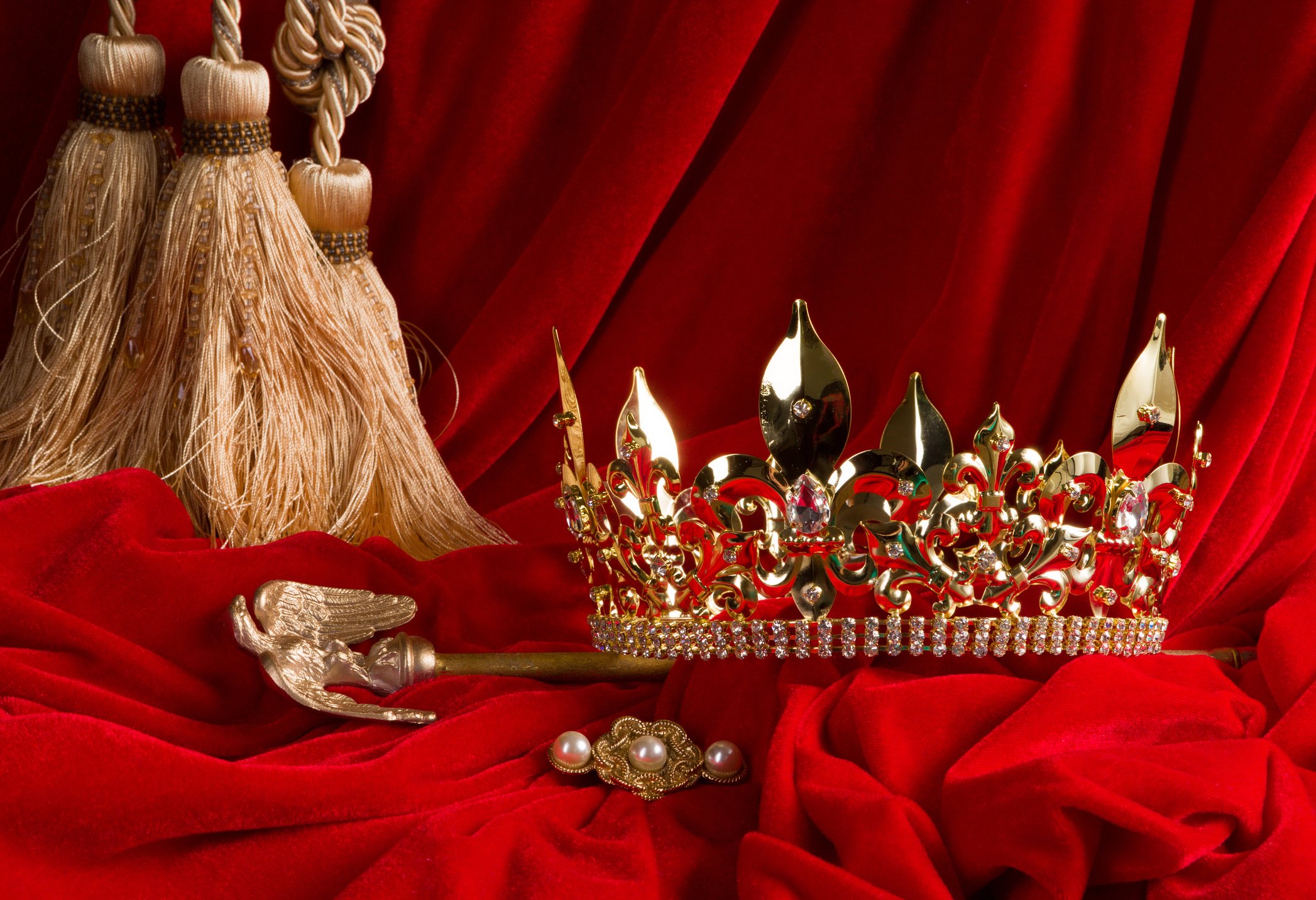 A crown and scepter arranged on red velvet. 