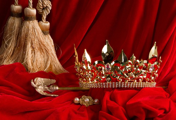 A crown and scepter arranged on red velvet. 