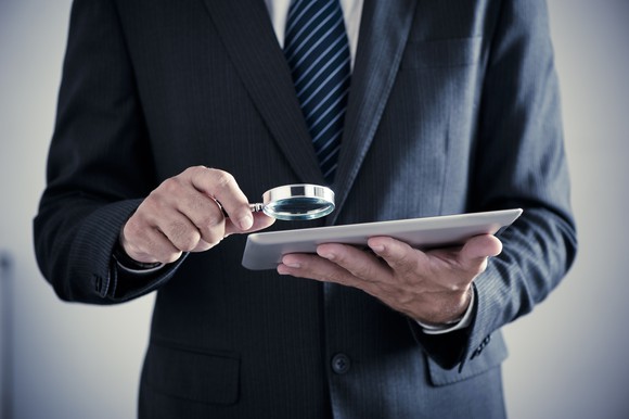 A businessman holding a magnifying glass up to a tablet.