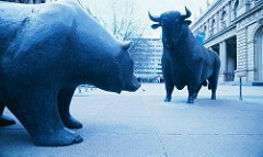 Blue-tint photo of statues of a bull and a bear arranged so as they are facing off against one another, with urban buildings in the background.