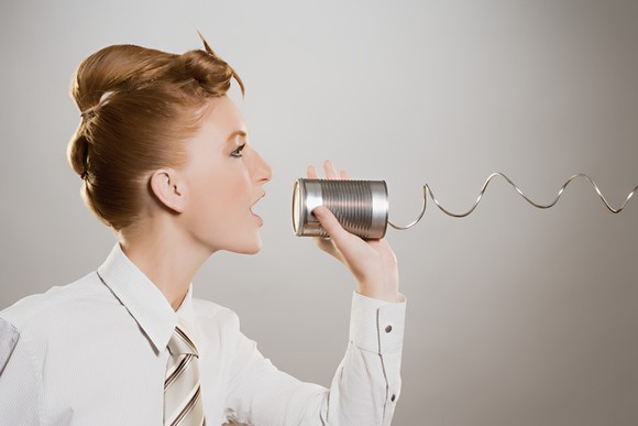 Redheaded woman in business attire speaking through a tin-can phone to an unseen person