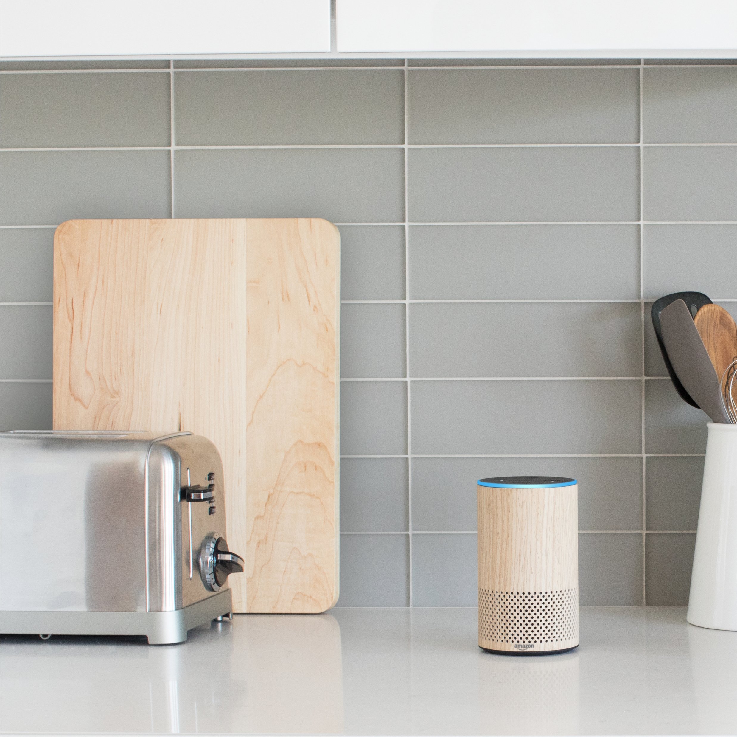 An Echo with oak finish displayed on a kitchen counter with cutting board and toaster.