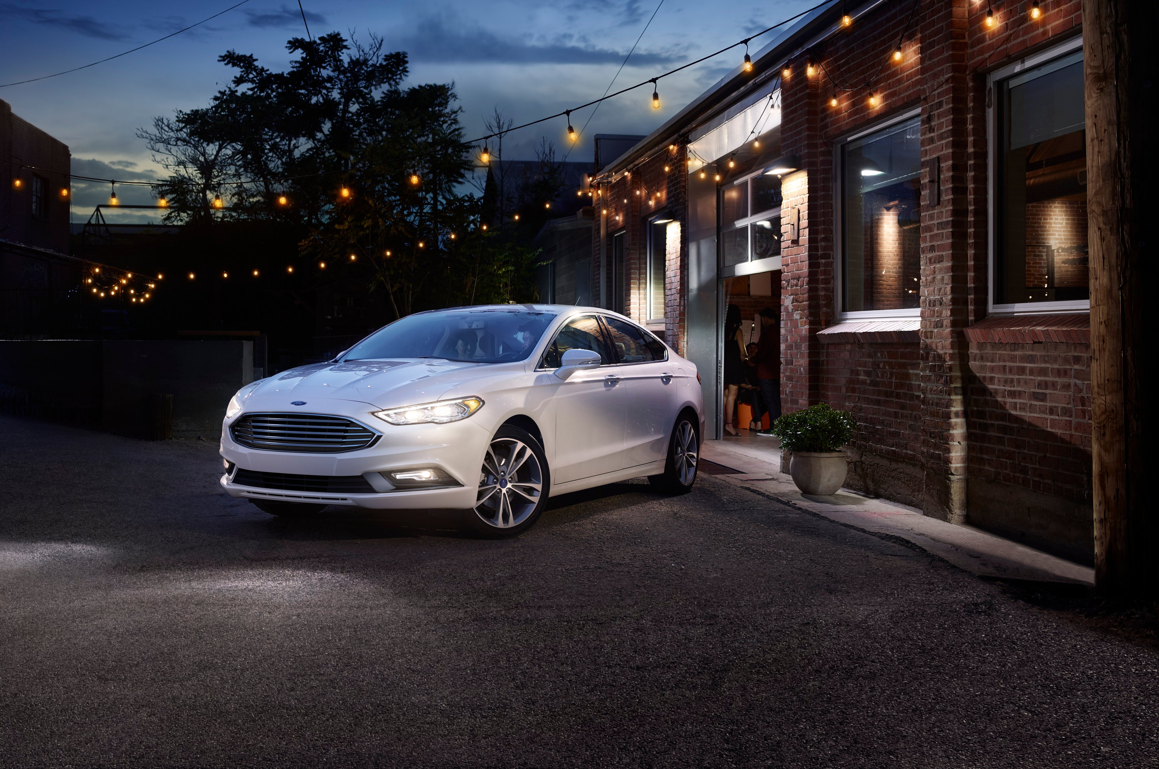 A white Ford 2017 Fusion parked in front of a brick building at night