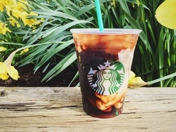 A Starbucks iced coffee siting on a wooden surface, with daffodils in the background.