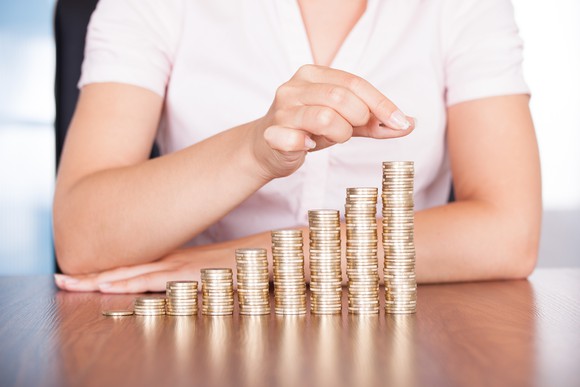 Woman in a white shirt, stacking coins in piles of rising height on a table.