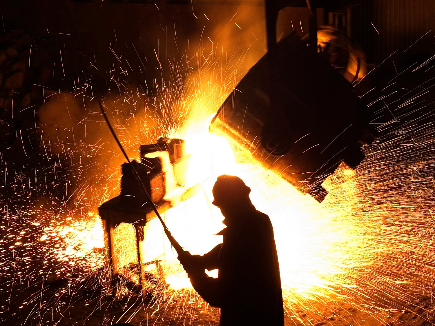 Steel worker in a foundry with sparks flying in the background. 