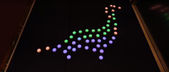 50 small robots arranged to form a multi-colored dinosaur on a black table.