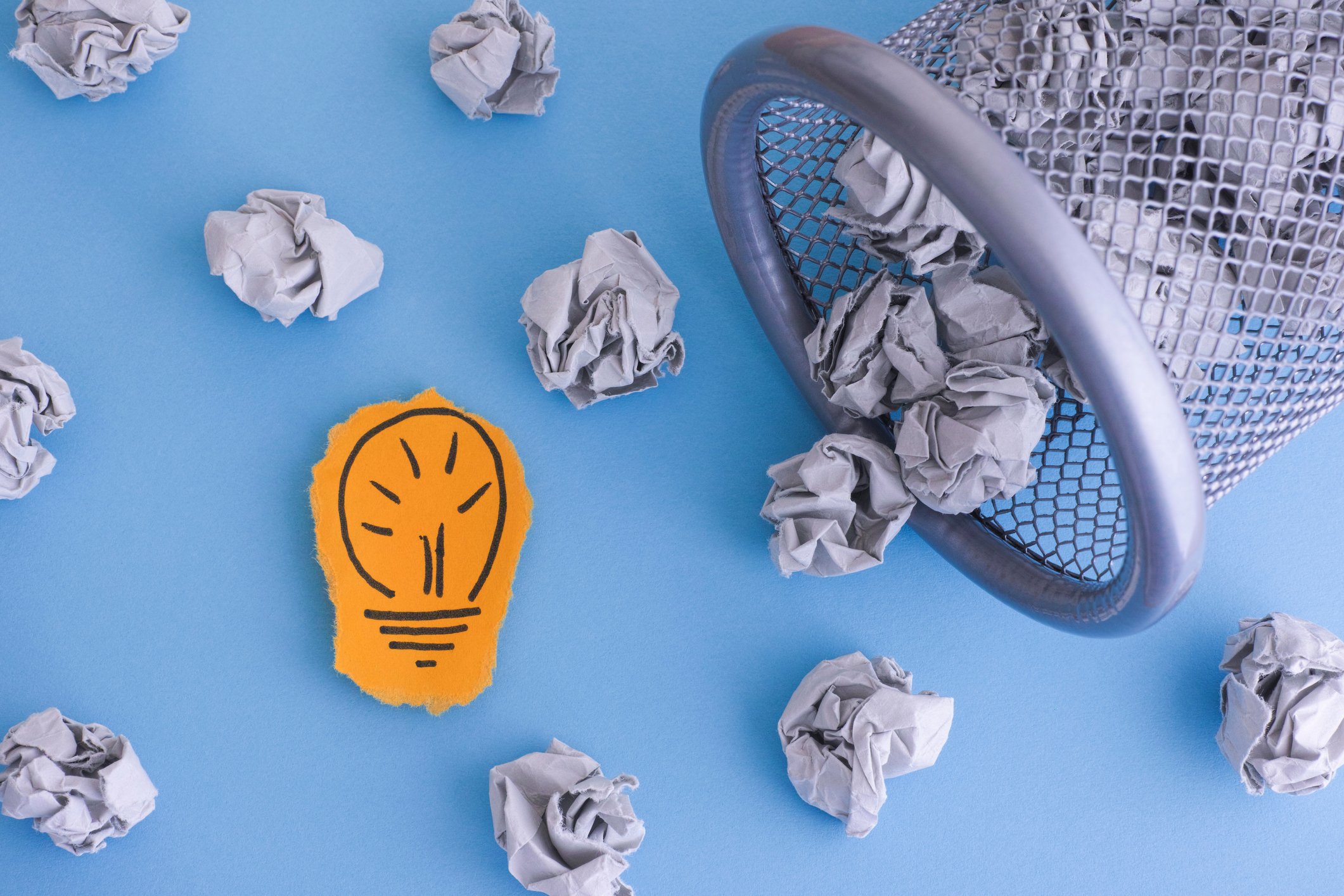 Picture of light bulb on paper next to crumpled paper spilled out of trash can