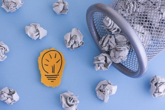 Picture of light bulb on paper next to crumpled paper spilled out of trash can