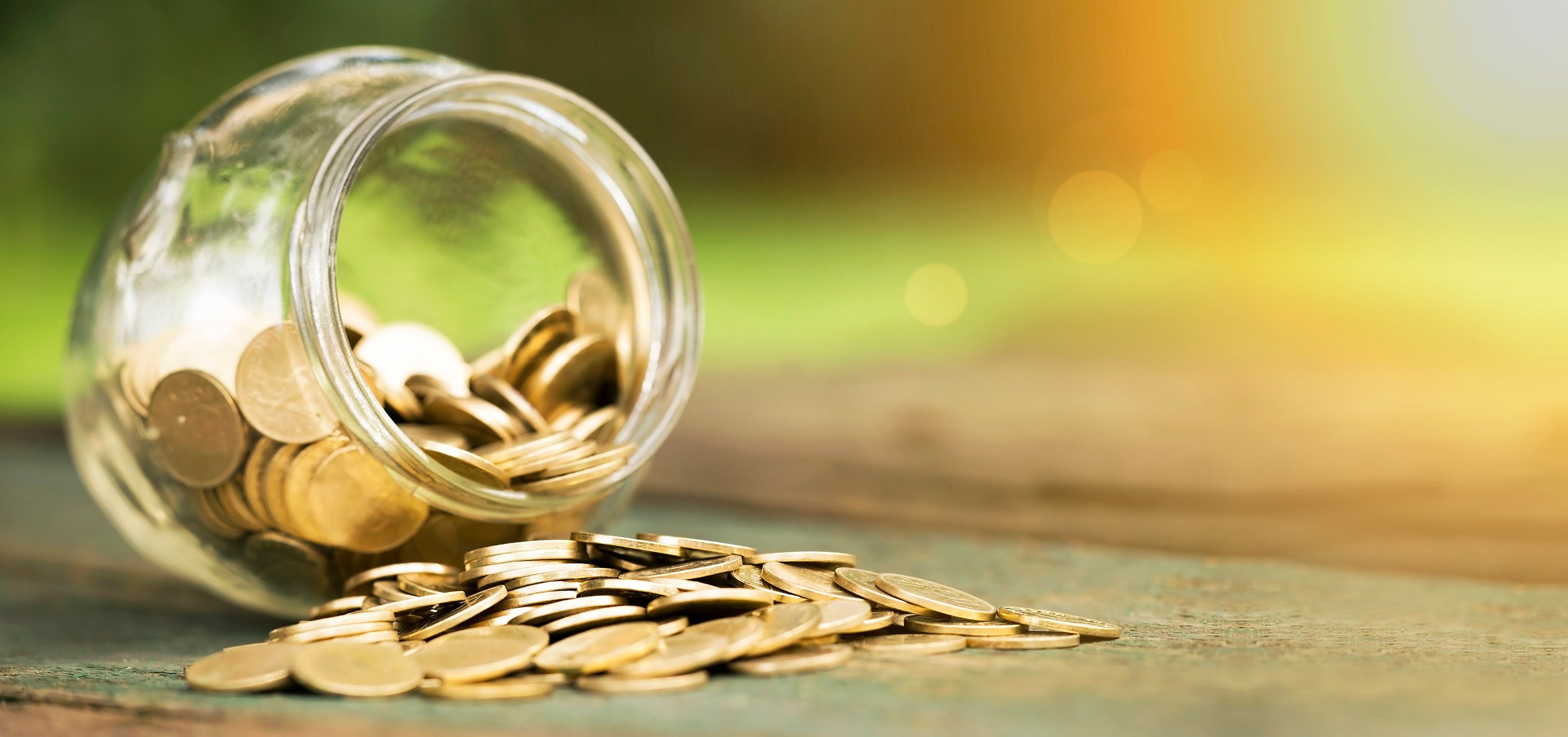 Gold coins spilling from a glass jar on the ground. 