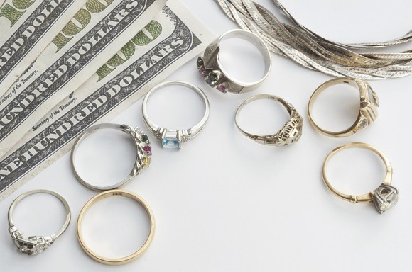 $100 bills, a necklace, and eight rings on a white background.
