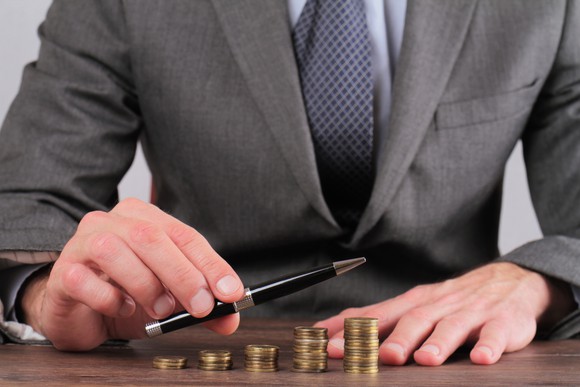 Stack of progressively larger coins on a desk while a business person points in the direction of the coin stacks.