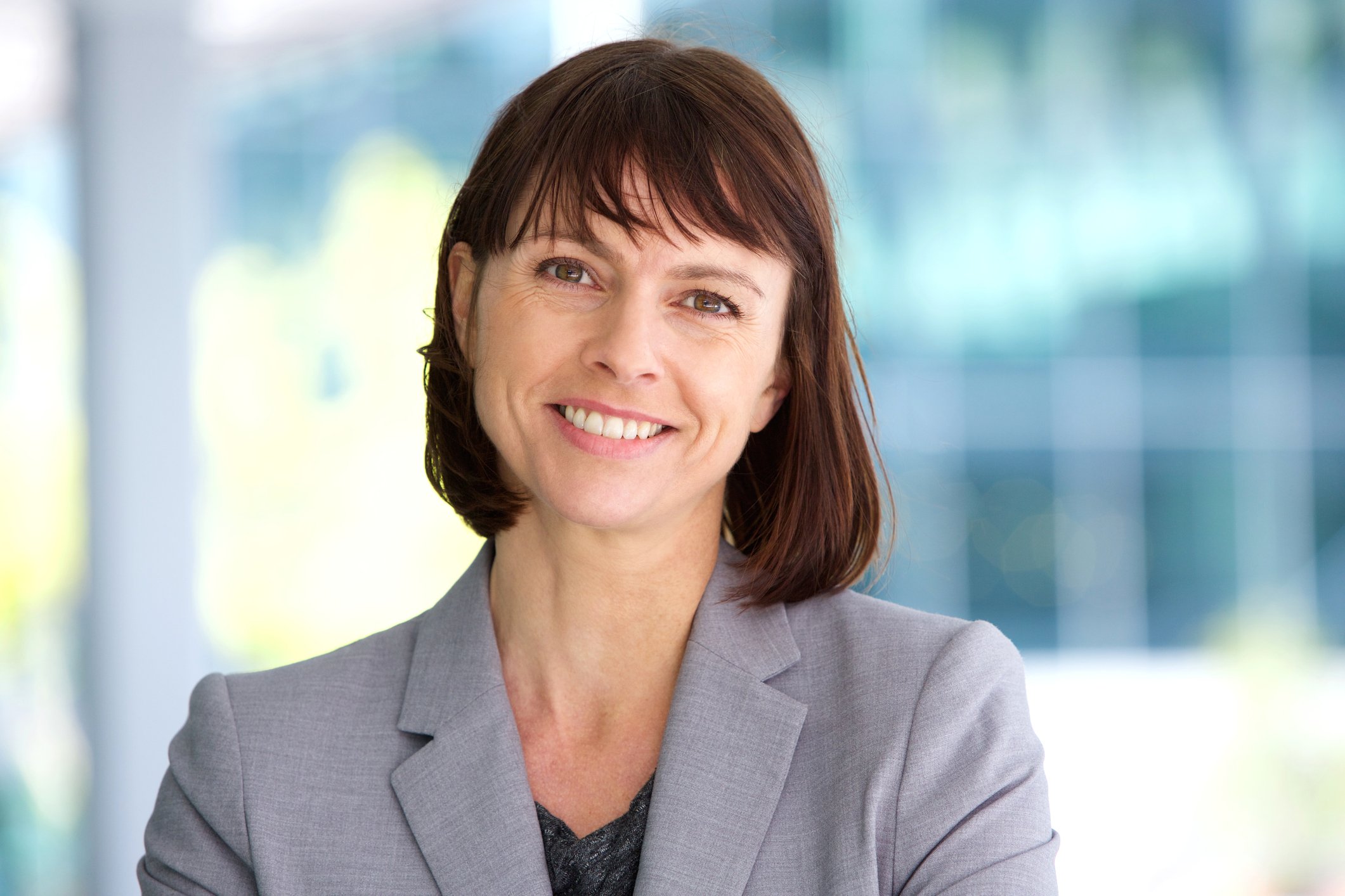 A smiling woman outdoors, wearing a gray blazer.