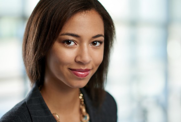 A smiling woman wearing a necklace and a gray pinstriped blazer.