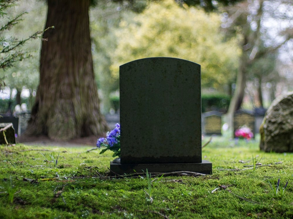 Gravestone with purple flowers in a graveyard.