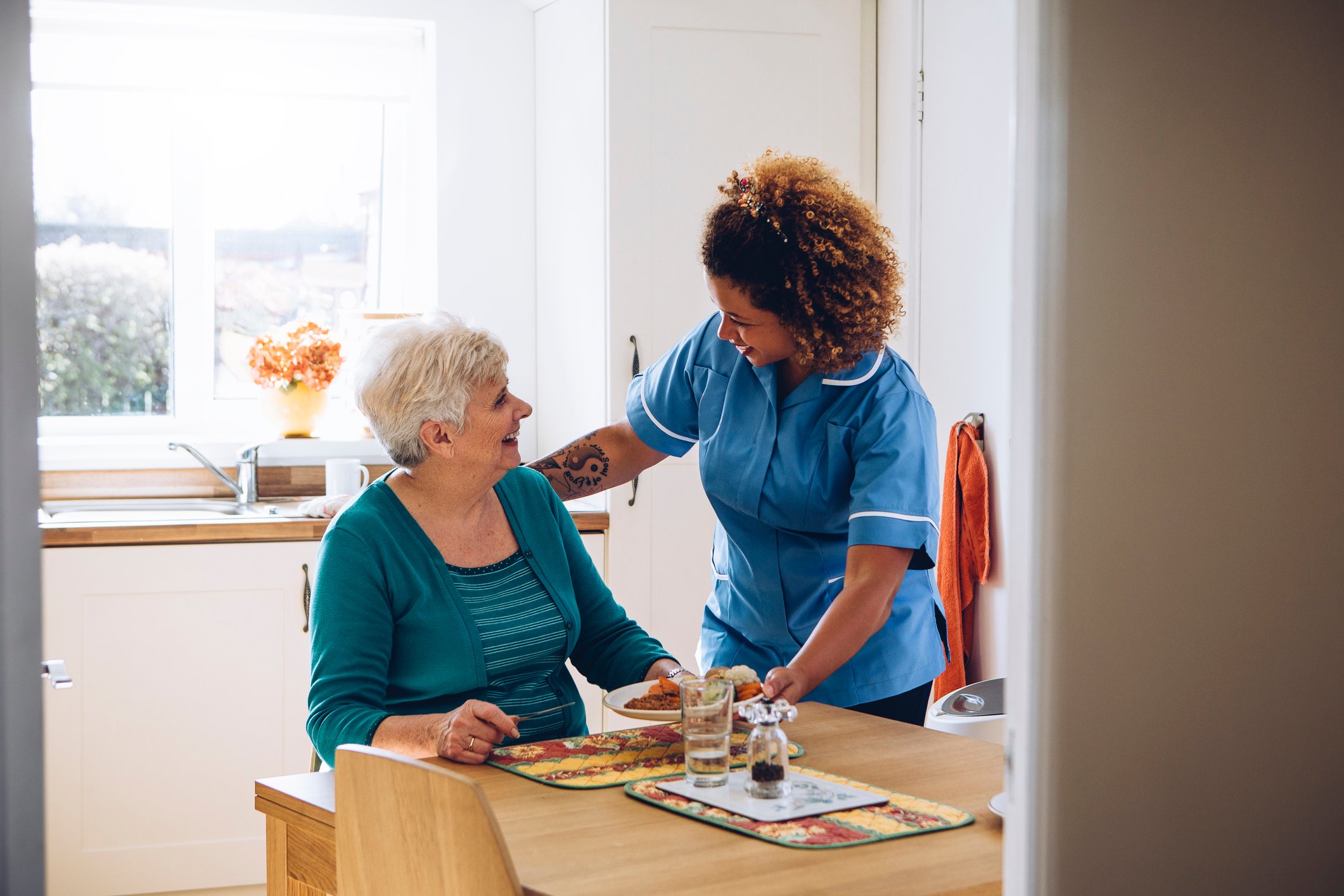 Woman in scrubs helping older woman at the table