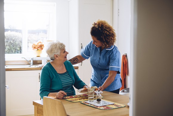 Woman in scrubs helping older woman at the table