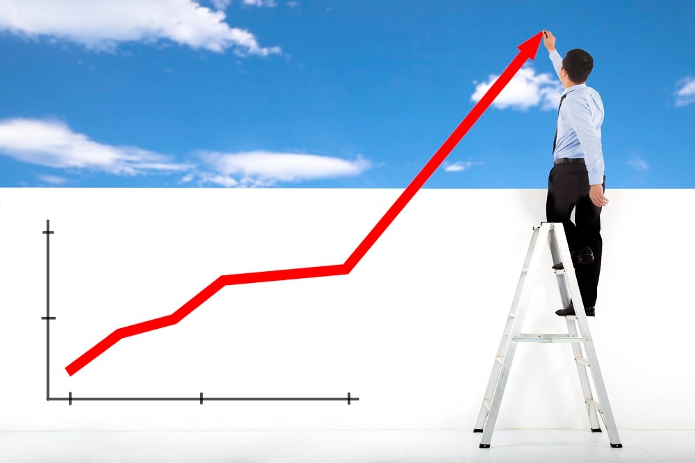 Man standing on ladder drawing a chart going up. 