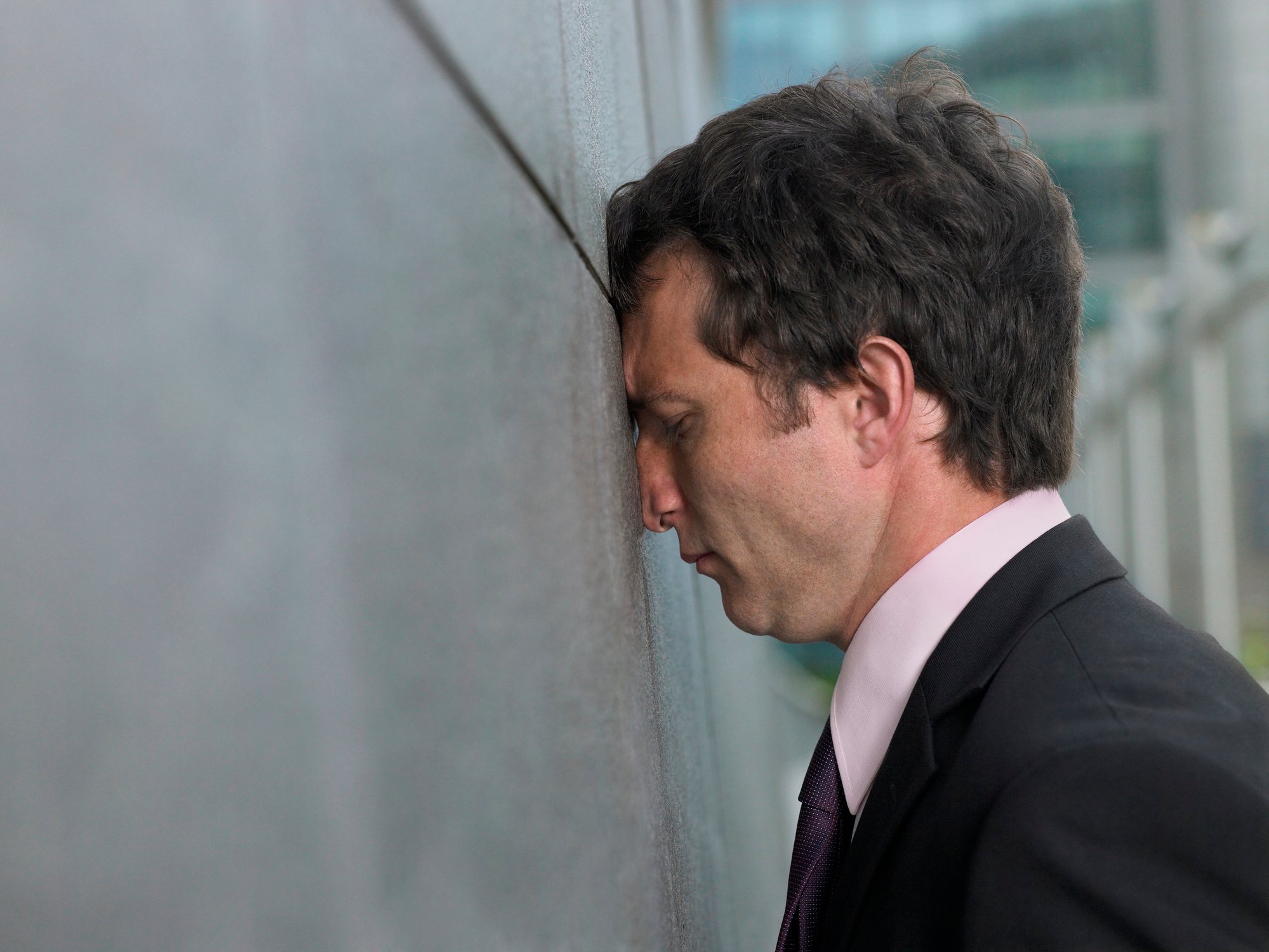 Business man leans his head against the wall.