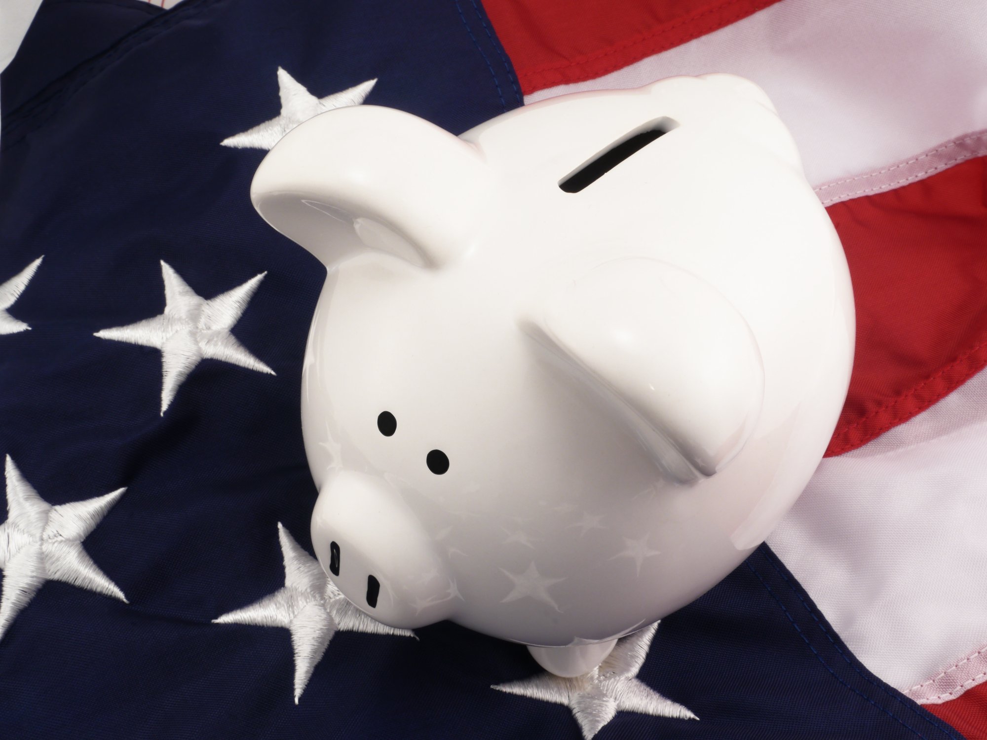 A white piggy bank sits on top of an American flag.