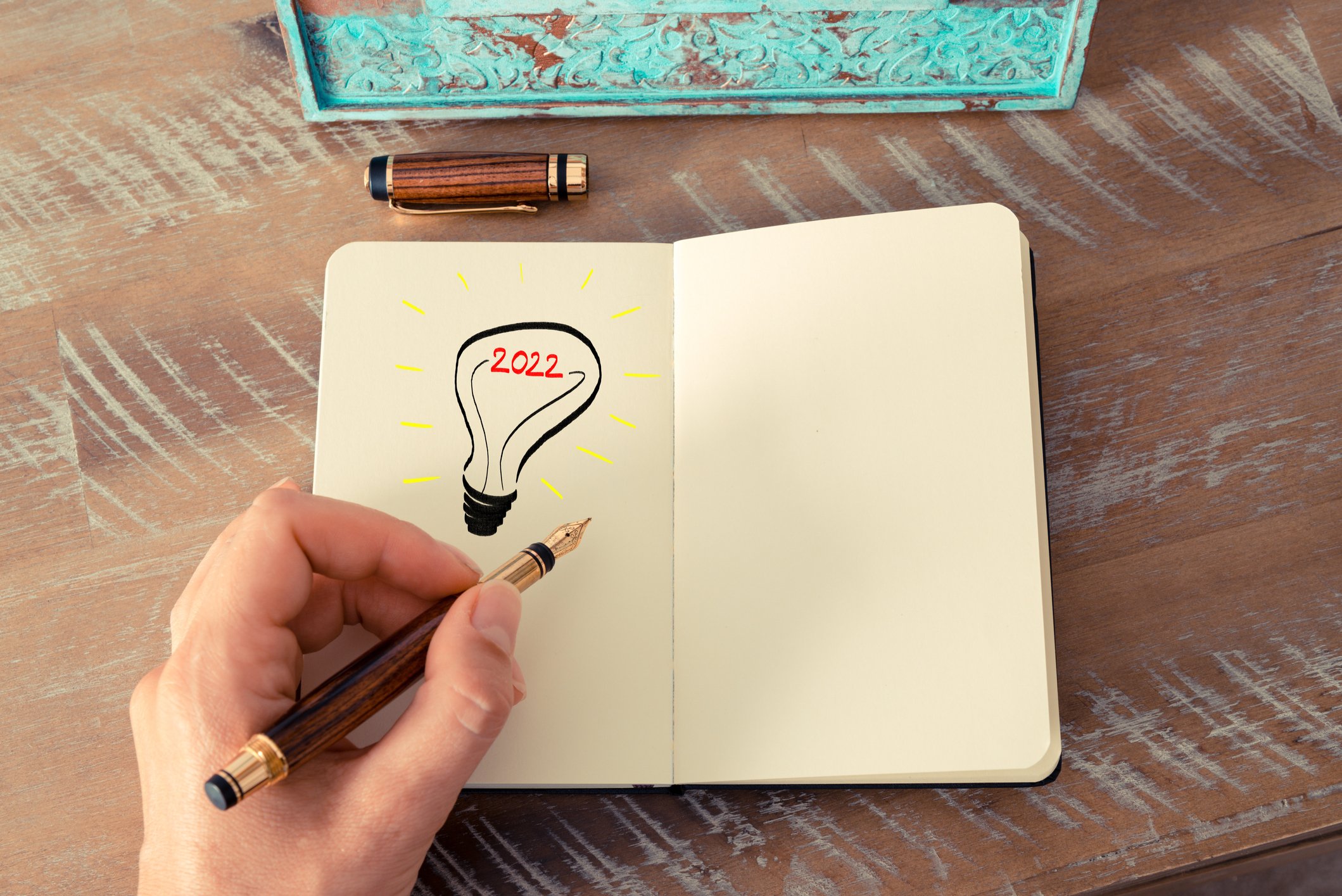 Hand holding pen over notepad with picture of light bulb with 2022 drawn on it