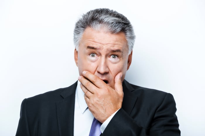 A shocked baby boomer in a suit with his hand over his mouth.