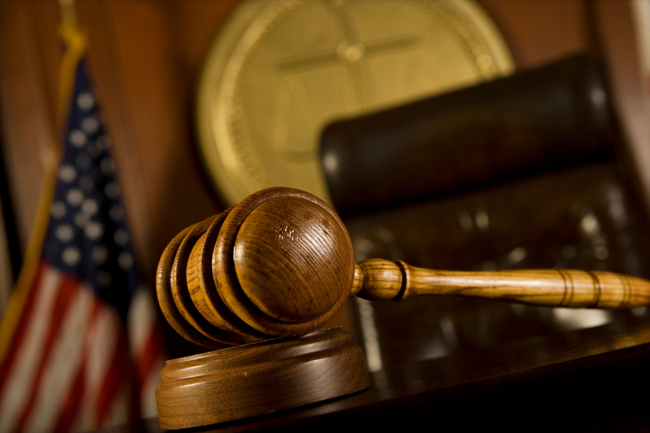 A judge's gavel, chair, and flag in view inside of a courtroom. 