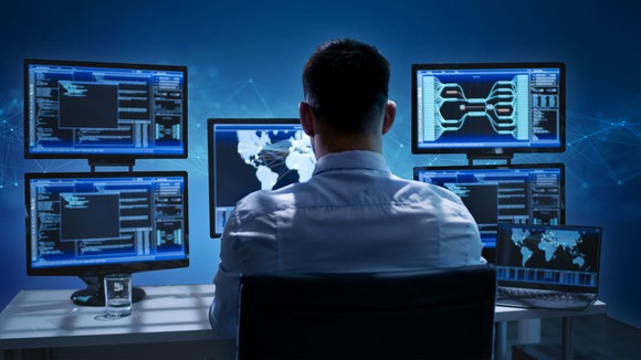 Man looking at several computer screens.