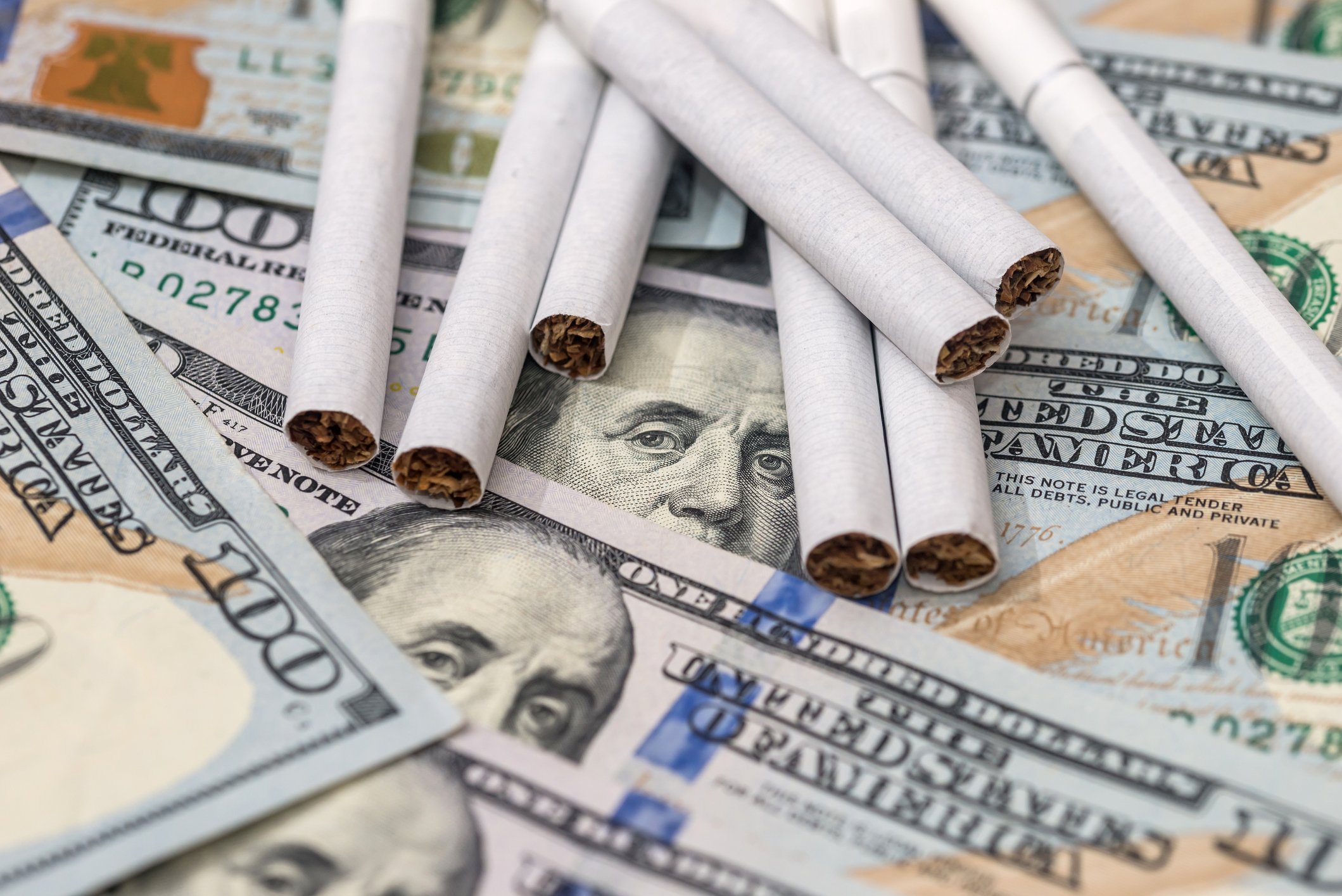 Cigarettes laid out on top of a pile of $100 bills.