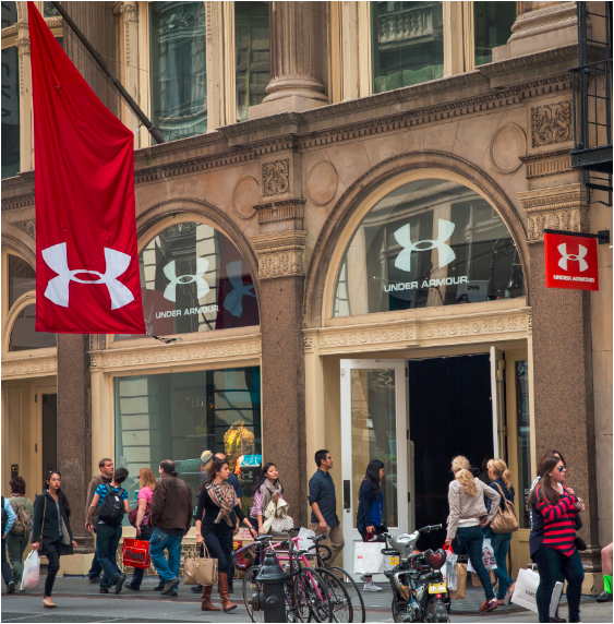 The outside of Under Armour's New York's Soho store with many pedestrians with shopping bags. 