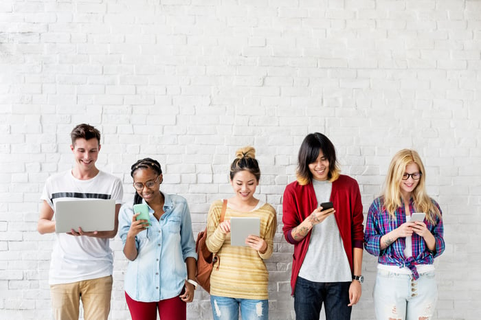 Five people standing in front of a wall and using their mobile devices. 