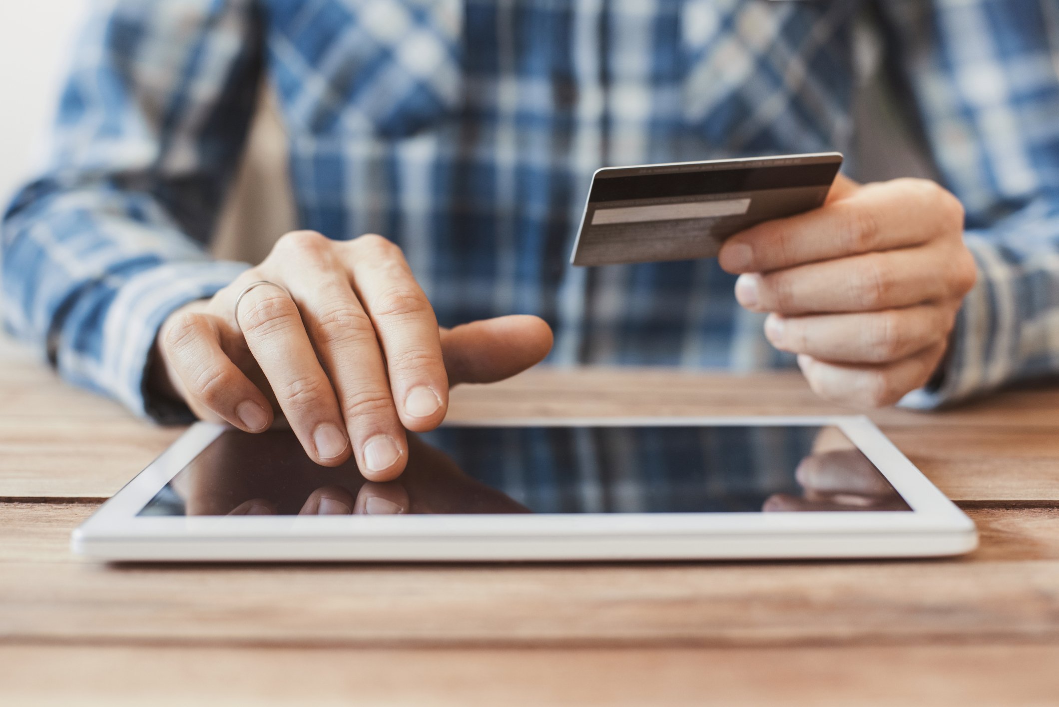 A man scrolling along a digital tablet while holding a credit card in his other hand.