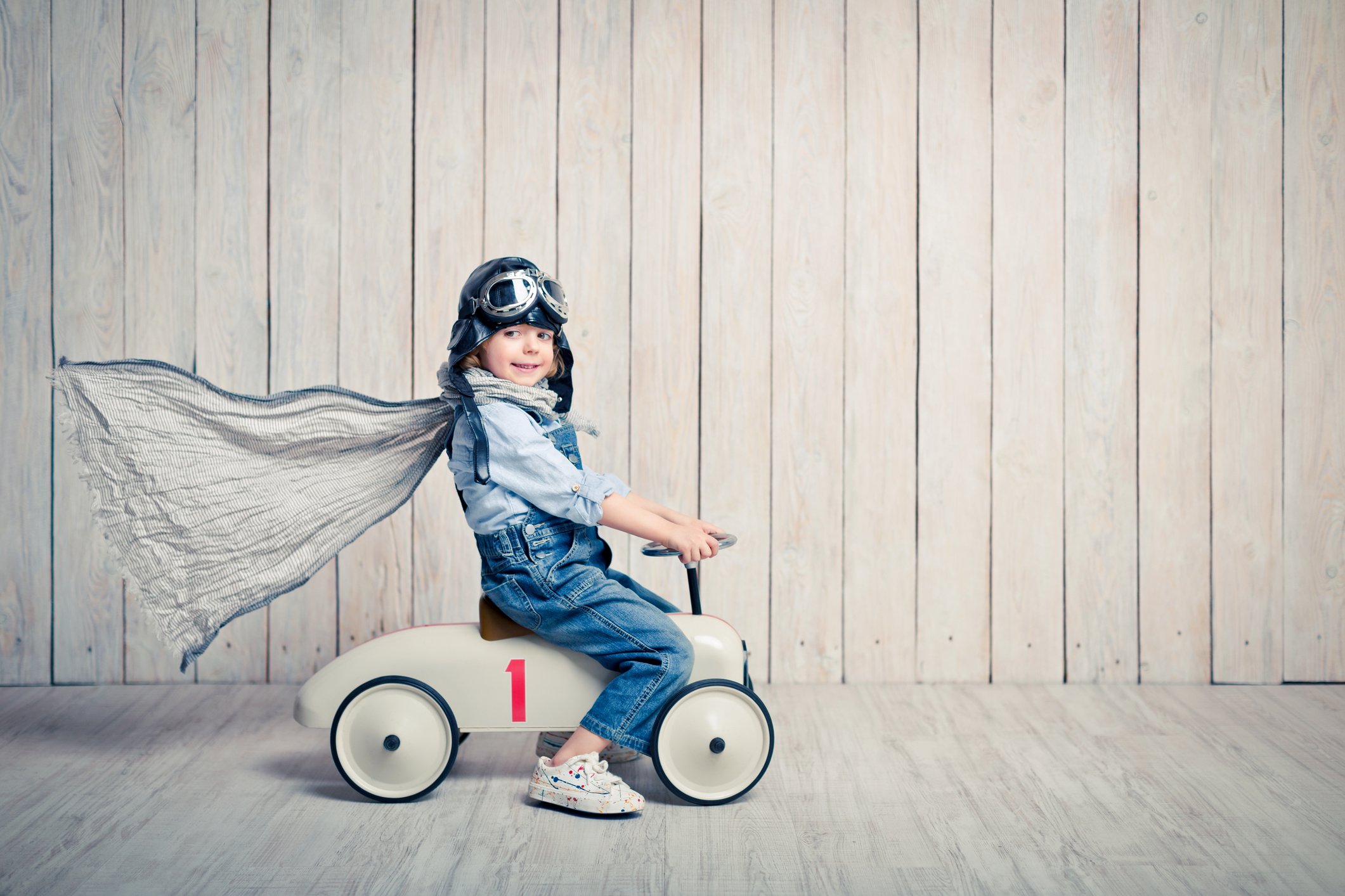 A small boy rides a toy car with a cape on