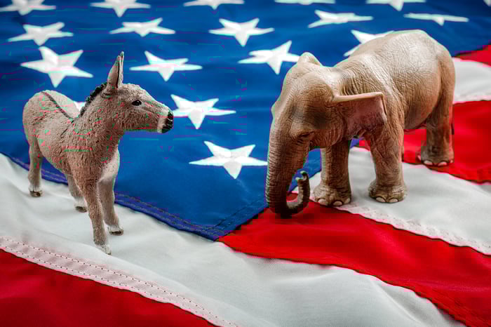 A donkey and elephant standing on a U.S. flag. 