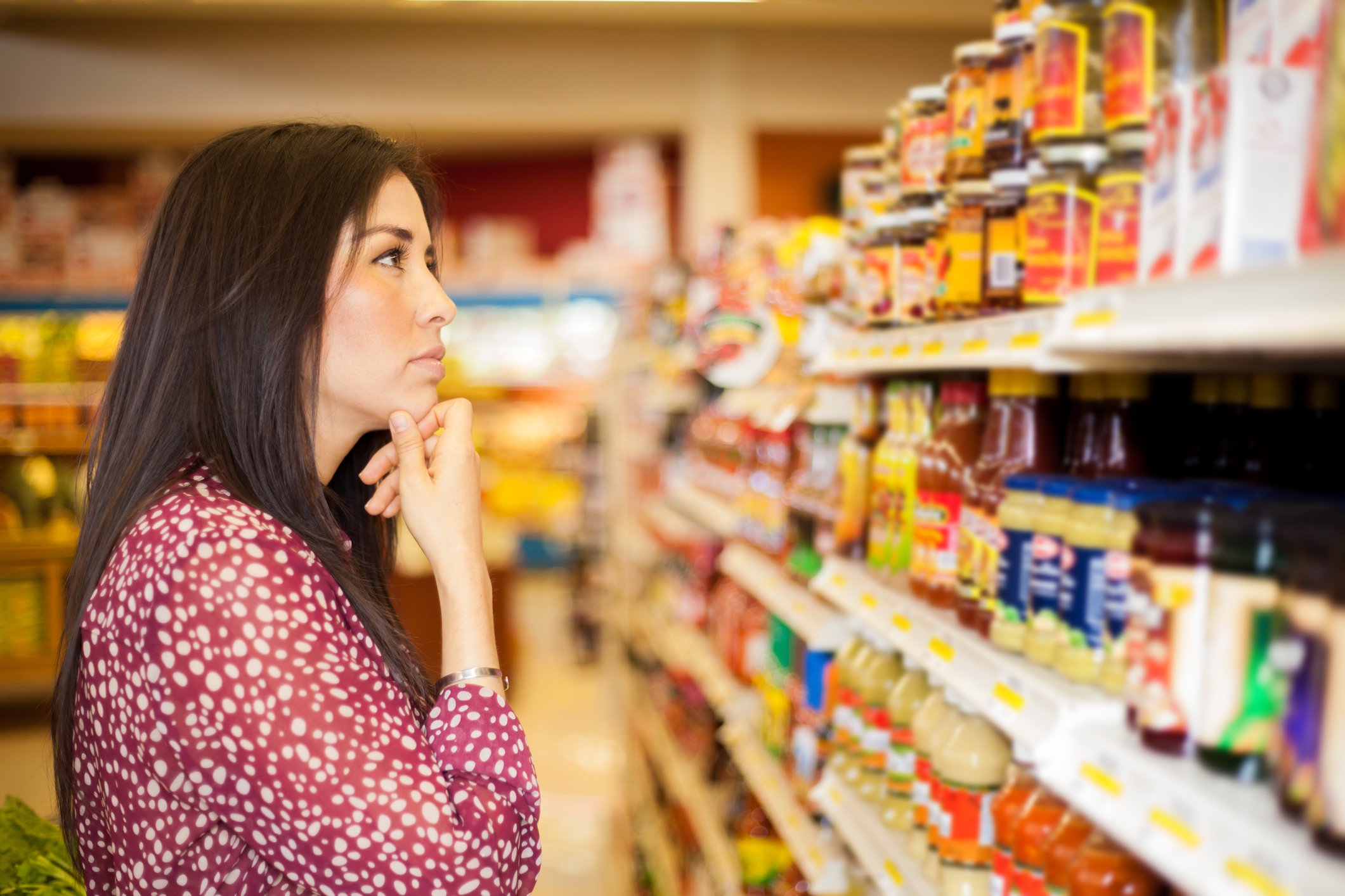Woman standing in an aisle at a grocery store trying to decide what to buy.