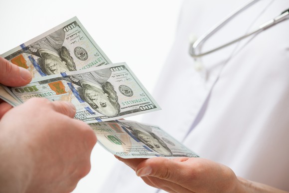 Person handing three $100 bills to a doctor.