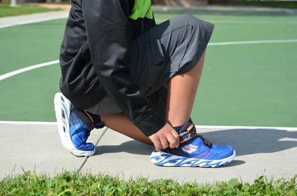 Someone adjusting his shoes at an outdoor basketball court.