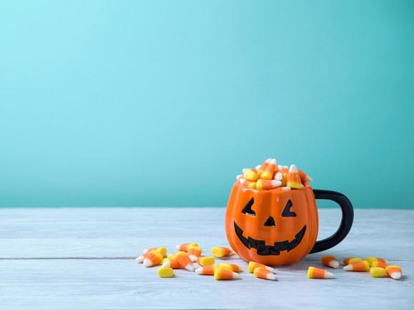A jack-o-lantern mug is filled with candy corn.