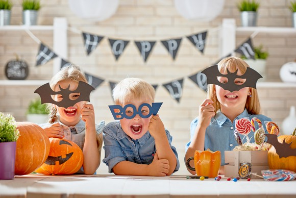 Kids pose with masks in front of a "happy Halloween" sign.