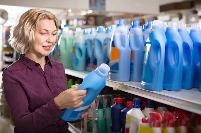 A woman choosing laundry detergent from a store shelf.